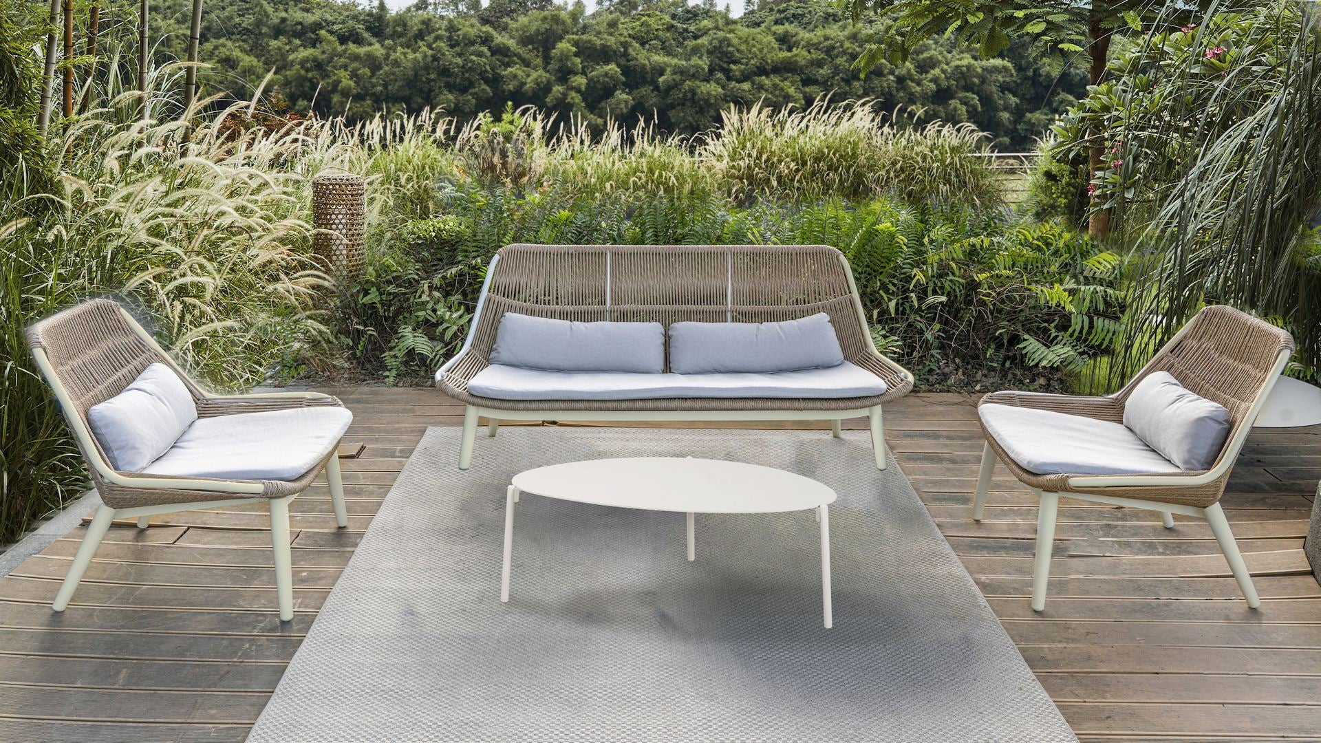 Die Celeste Loungegruppe in einem idyllischen Garten, bestehend aus einer Sitzbank, zwei Fauteuils und einem Couchtisch, umgeben von üppigem Grün und mit stilvollen, bequemen Kissen ausgestattet, bietet sie einen eleganten Entspannungsbereich im Freien.