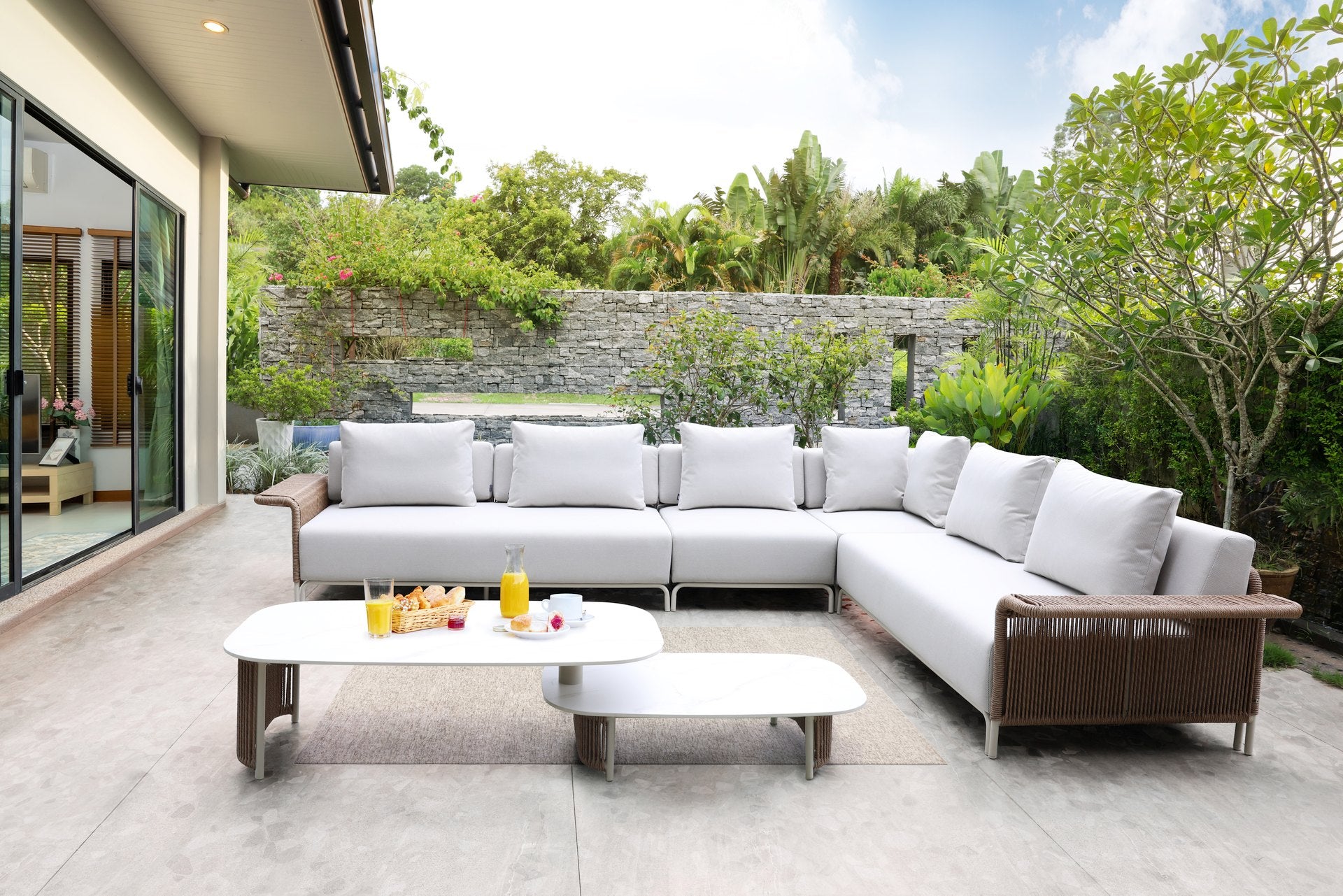 Moderne Cassidy Loungegruppe mit Eckbank, Fauteuil und multifunktionalem Couchtisch, eingebettet in einen grünen Garten mit vielseitigen Sitzoptionen und erweiterbarem Mittelelement, umgeben von üppiger Vegetation.