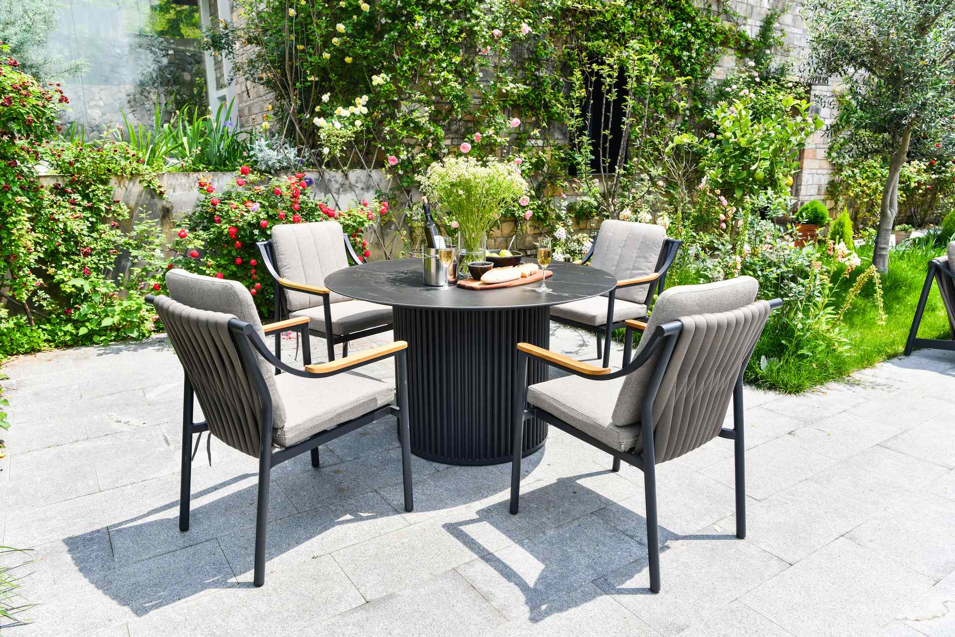 Tischgruppe Cassiopeia mit rundem Gartentisch aus Sinterstone und 6 Armstühlen Tristan mit Teakholz-Details.