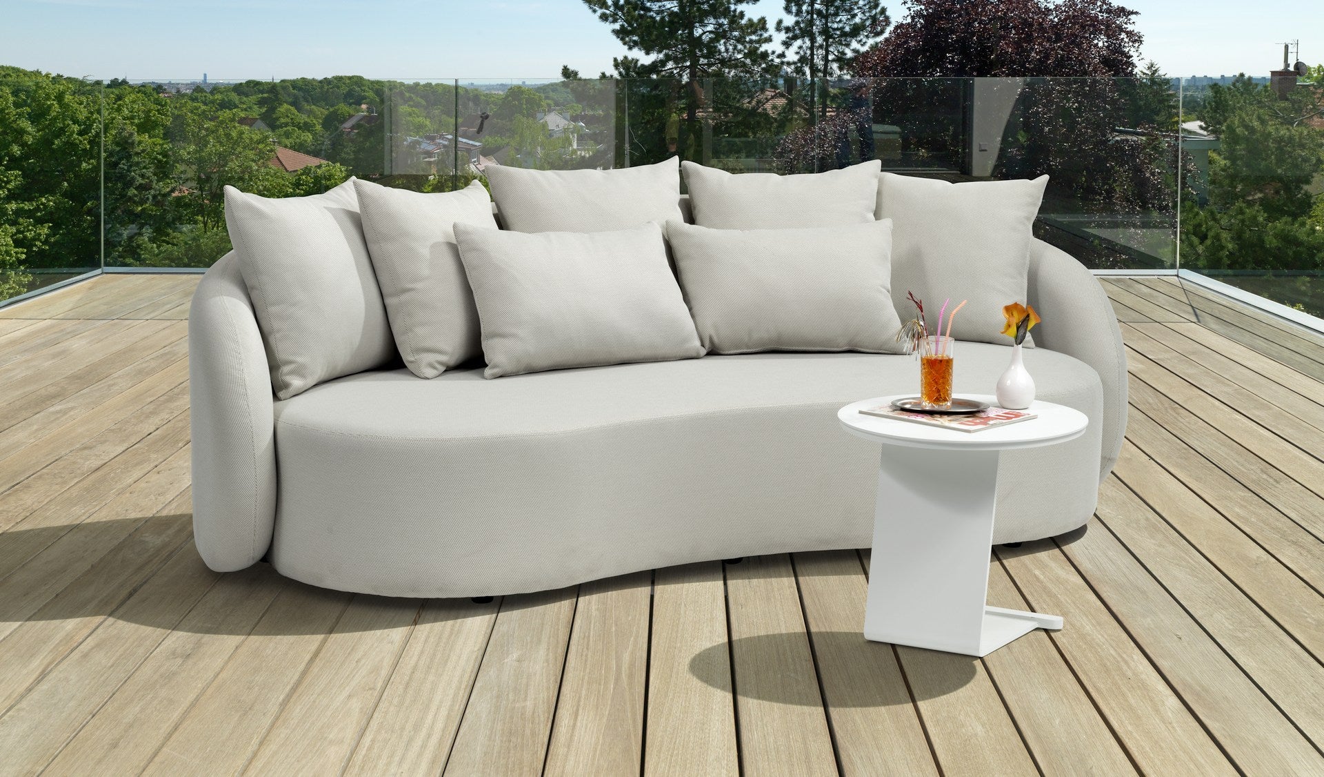Modernes Letizia Garten-Sofa in Creme mit wasserabweisendem Axroma-Stoff und zahlreichen Rückenkissen, arrangiert auf einer Holzterrasse mit einem eleganten weißen Beistelltisch, präsentiert als ideale Ergänzung für stilvolles Outdoor-Entspannen.