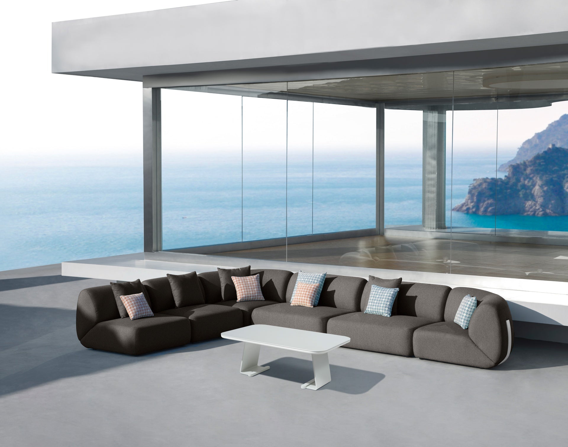 Modulare Monique Loungeelemente im Außenbereich mit weißem Aluminiumgestell und robustem Axroma-Stoff, arrangiert auf einer modernen Terrasse mit atemberaubender Meereskulisse.